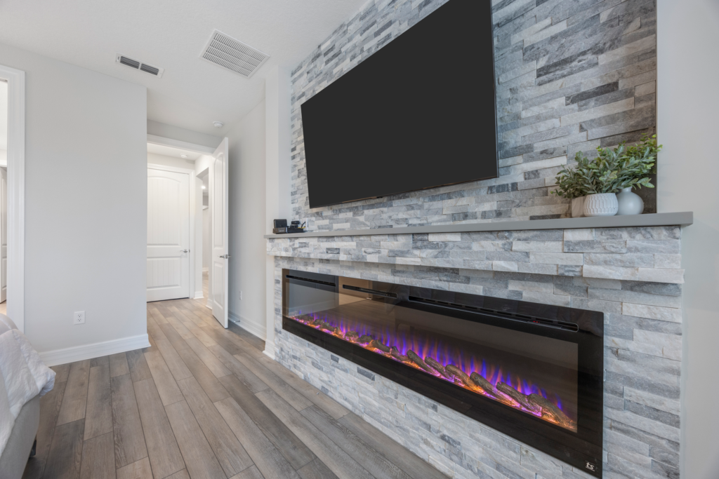 Stone fireplace wall with linear electric fireplace in the primary suite at 94 Hickory Pine Drive